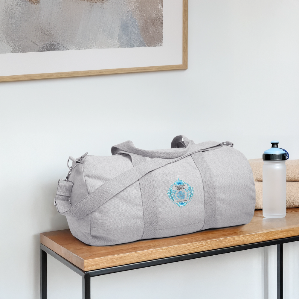 Graue sapeco Halschakra-Sporttasche mit hellblau-türkisem Lotusmotiv auf einer Bank – für Yoga, Fitness, Reisen und Alltag.