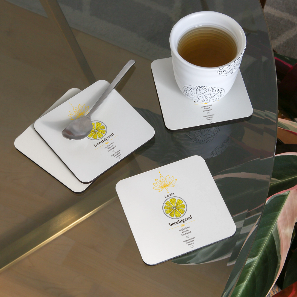 Weiße sapeco Untersetzer mit gelbem Solarplexuschakra-Motiv „Ich bin beruhigend“ mit Tasse auf Glastisch